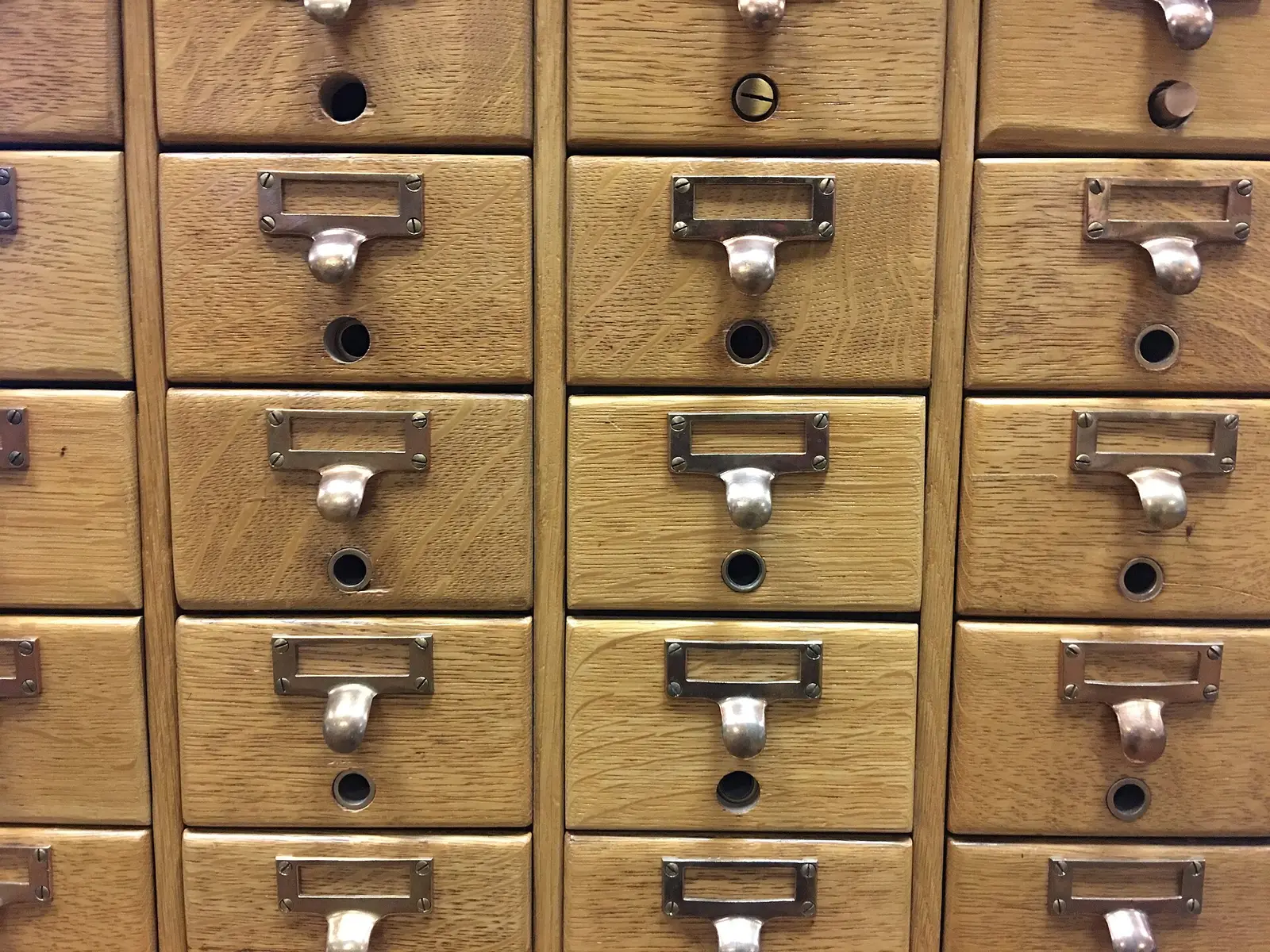 Rows of wooden library card catalog drawers with brass label holders and pull handles