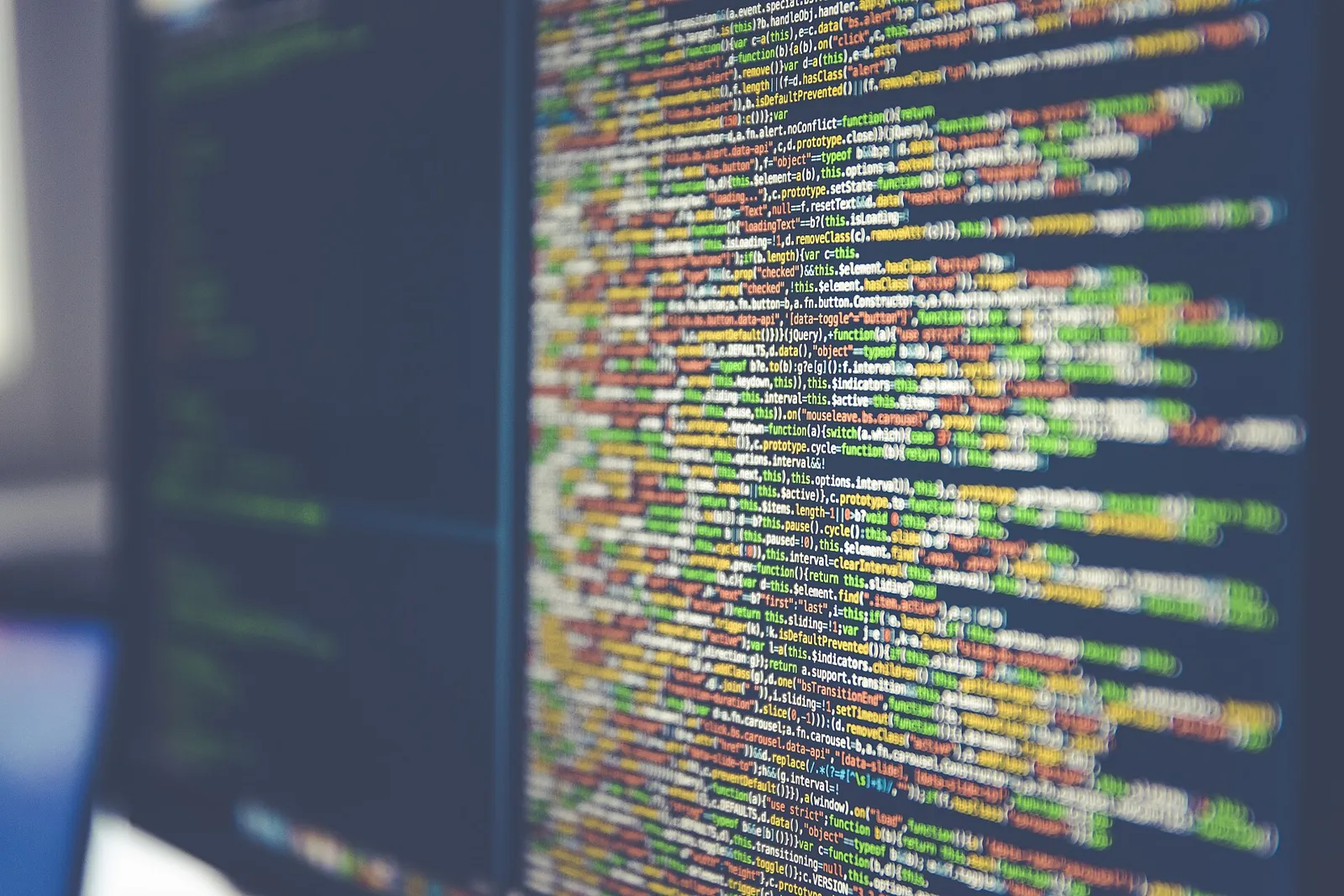 Blurred close-up of colorful JavaScript source code on a dark computer monitor
