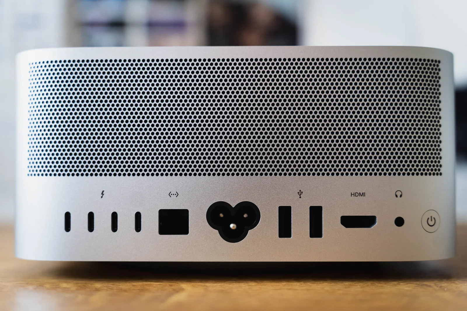 The rear panel of an Apple Mac Studio on a wooden desk, showing a perforated vent grille above four Thunderbolt ports, Ethernet, power, USB-A, HDMI, and a headphone jack