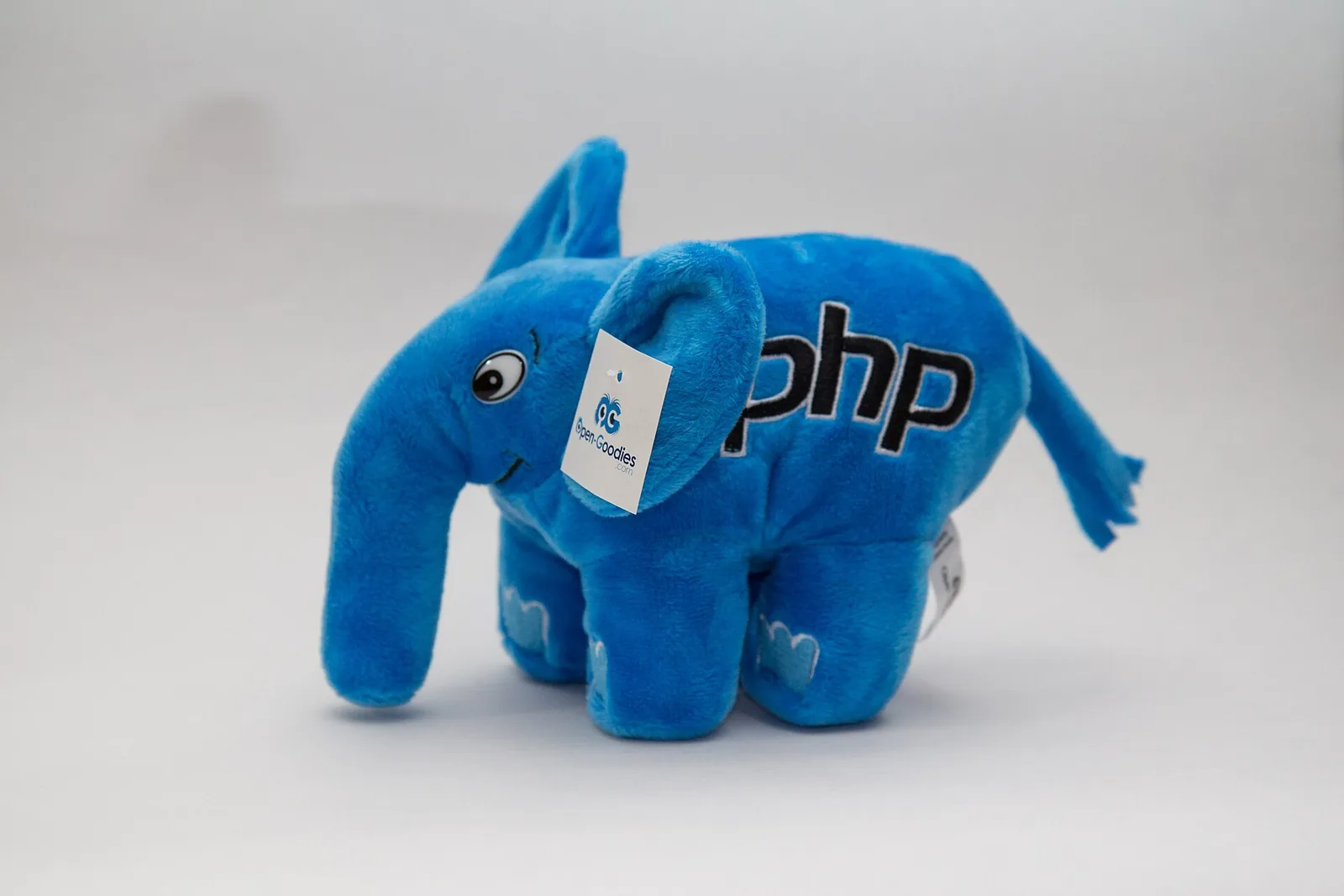 A blue plush PHP elephant with an Open Goodies tag on its ear, standing on a white background